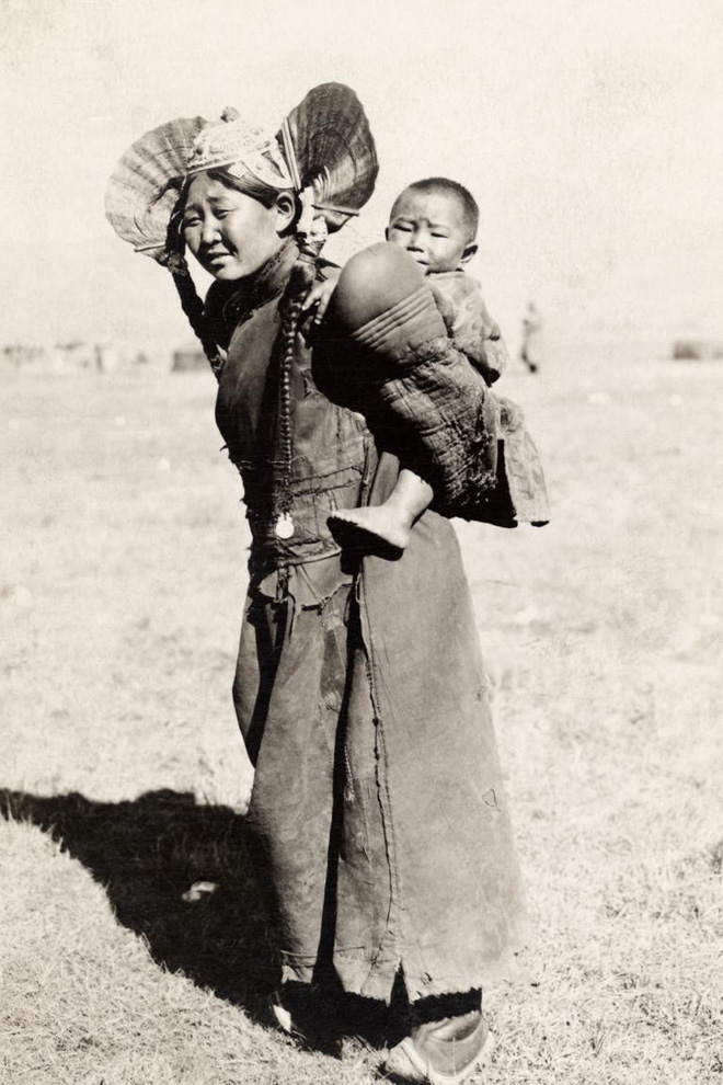 Một người mẹ trong trang phục truyền thống của người Mông Cổ đang địu con sau lưng giữa thảo nguyên rộng lớn. Ảnh chụp bởi Ethan C. Le Munyon.