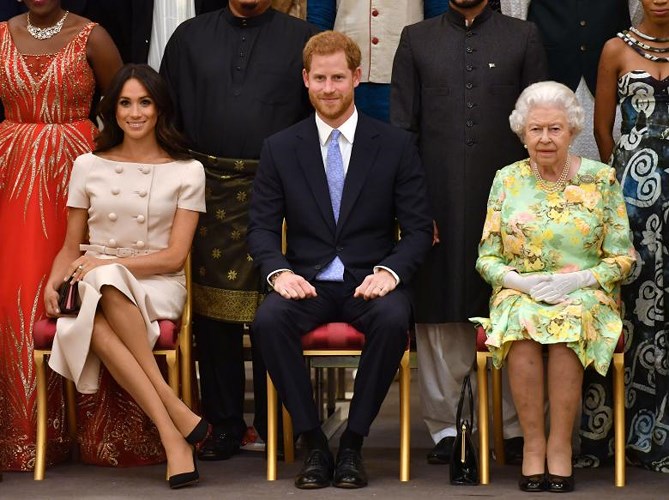 Công nương Meghan Markle diện một thiết kế đầm màu be phớt hồng trang nhã điểm xuyết chi tiết khuy cài to bản chụp ảnh cùng Nữ hoàng Elizabeth và Hoàng tử Harry tại một buổi tiếp ở Cung điện Buckingham, ngày 26/6/2018.  