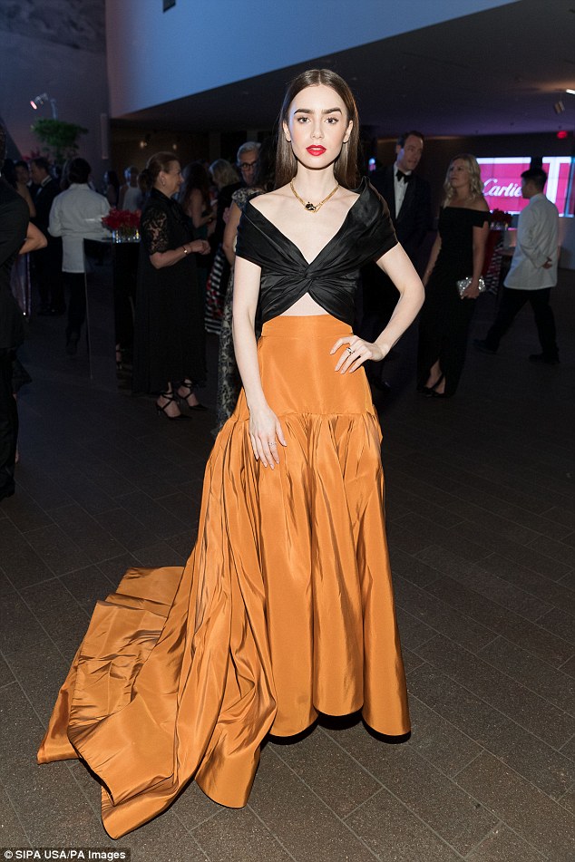 Diễn viên tài năng Lily Collins trông thật nổi bật và phá cách tại sự kiện với thiết kế áo crop-top đen cùng phần váy dài màu cam đất Terracotta.     