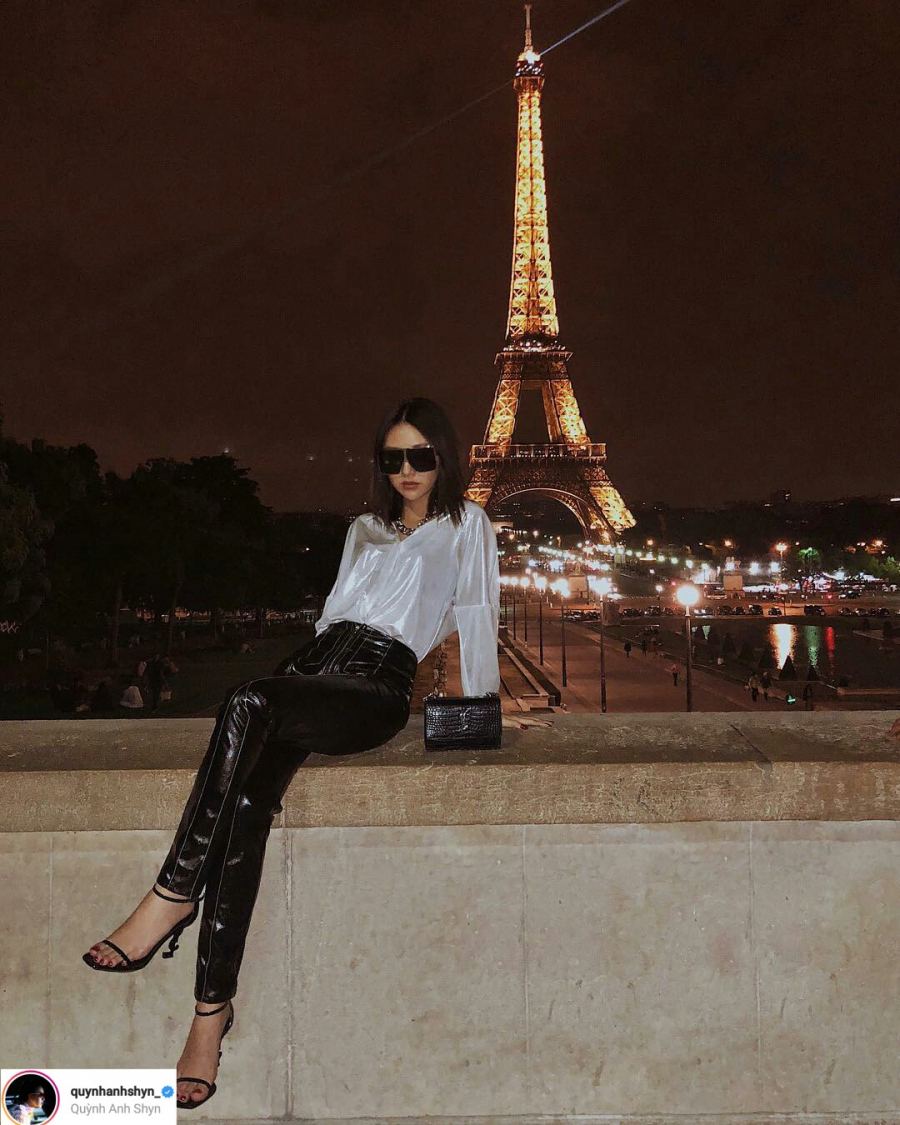 Quỳnh Anh Shyn tạo dáng cực ngầu bên tháp Eiffel với bộ trang phục chất liệu vải bóng. Lần này, thay vì chọn kính mắt tí hon quen thuộc, Quỳnh Anh Shyn chọn kính mắt vuông bản to. Đôi sandals quai mảnh và túi YSL cũng khiến cô nàng trở nên sành điệu hơn.    