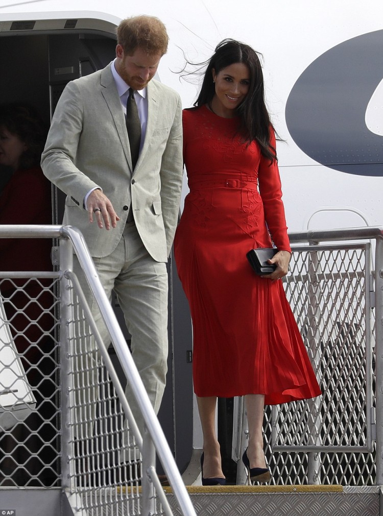Công tước và Nữ công tước xứ Sussex bước xuống máy bay tại phi trường Fua'amotu ở Nuku'alofa, thủ đô của Vương quốc Tonga hôm 25/10 trước sự tiếp đón của Công chúa Angelika Latufuipeka, người dân địa phương. Công nương Meghan nổi bật trong bộ đầm đỏ, giày cao gót đen và túi cầm tay thẫm màu.