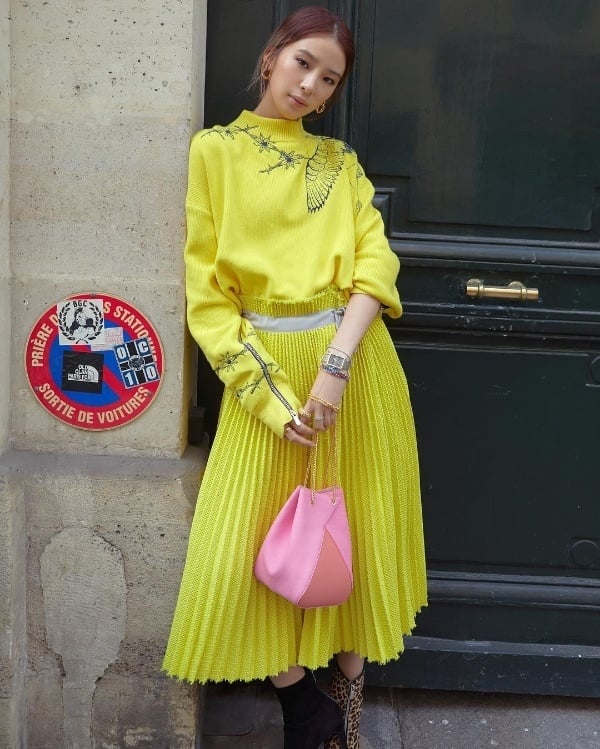 Yêu thích sự nổi bật, Irene Kim  tiếp tục chọn một bộ cánh tông màu vàng chanh bắt mắt bằng cách mix áo len oversized cùng chân váy midi. Chiếc túi xách màu hồng phấn trở thành điểm nhấn sáng giá cho set đồ của quý cô này.    