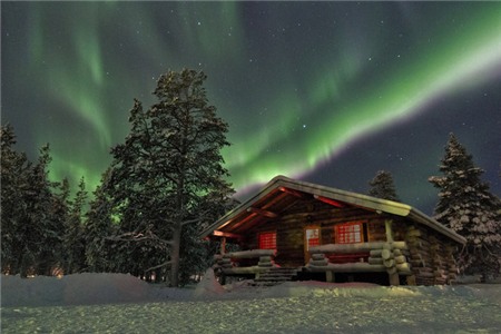 Ngôi nhà gỗ nổi bật dưới ánh sáng cực quang ở Lapland, Phần Lan.    