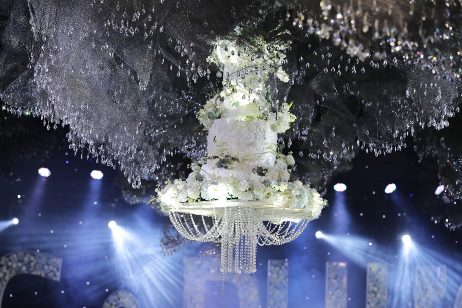Bánh cưới được treo ở chính giữa sân khấu, được tô điểm bằng hoa và những sợi dây pha lê, sẽ được từ từ đưa xuống khi cô dâu, chú rể thực hiện nghi lễ cắt bánh.