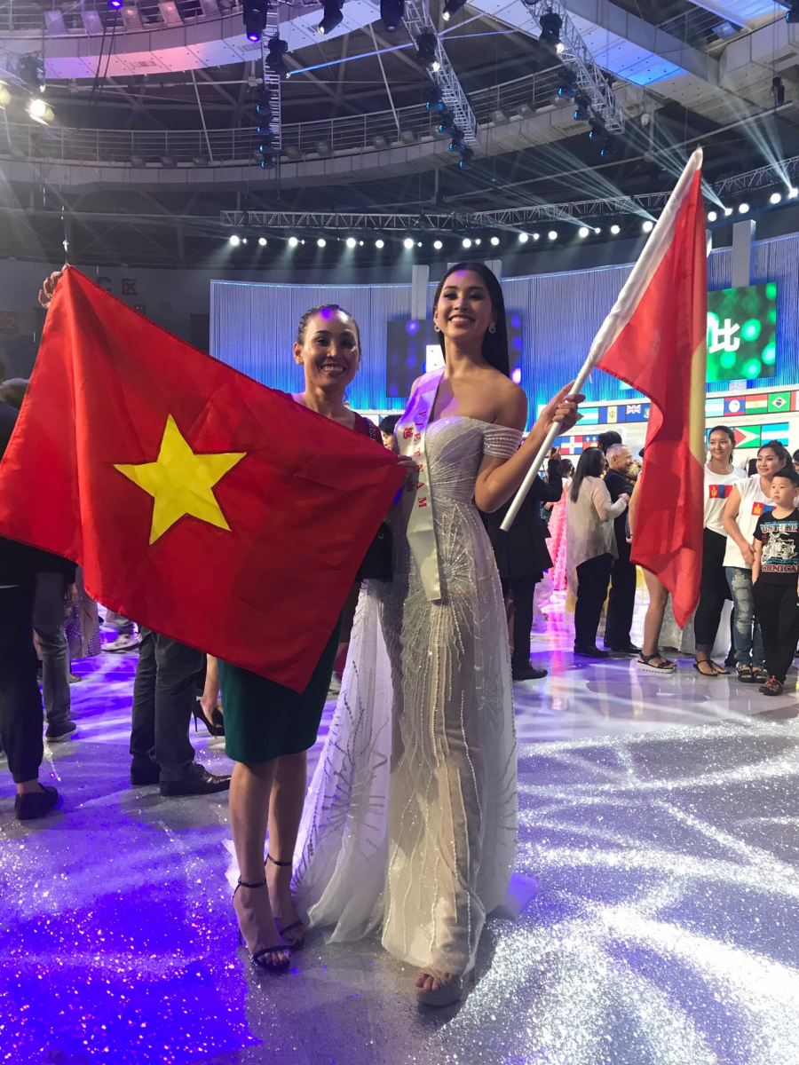 Hoa hậu vui vẻ bên mẹ trên sân khấu Miss World 2018 giương cao lá cờ Việt Nam.