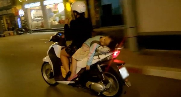 Mẹ lái xe bằng 1 tay mặc cho bé gái đang nằm dài sau yên xe ngủ