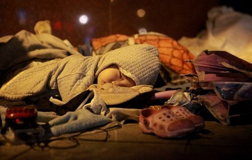 Một em be nằm ngủ trên tấm chăn mỏng trong đêm đông mưa lạnh.